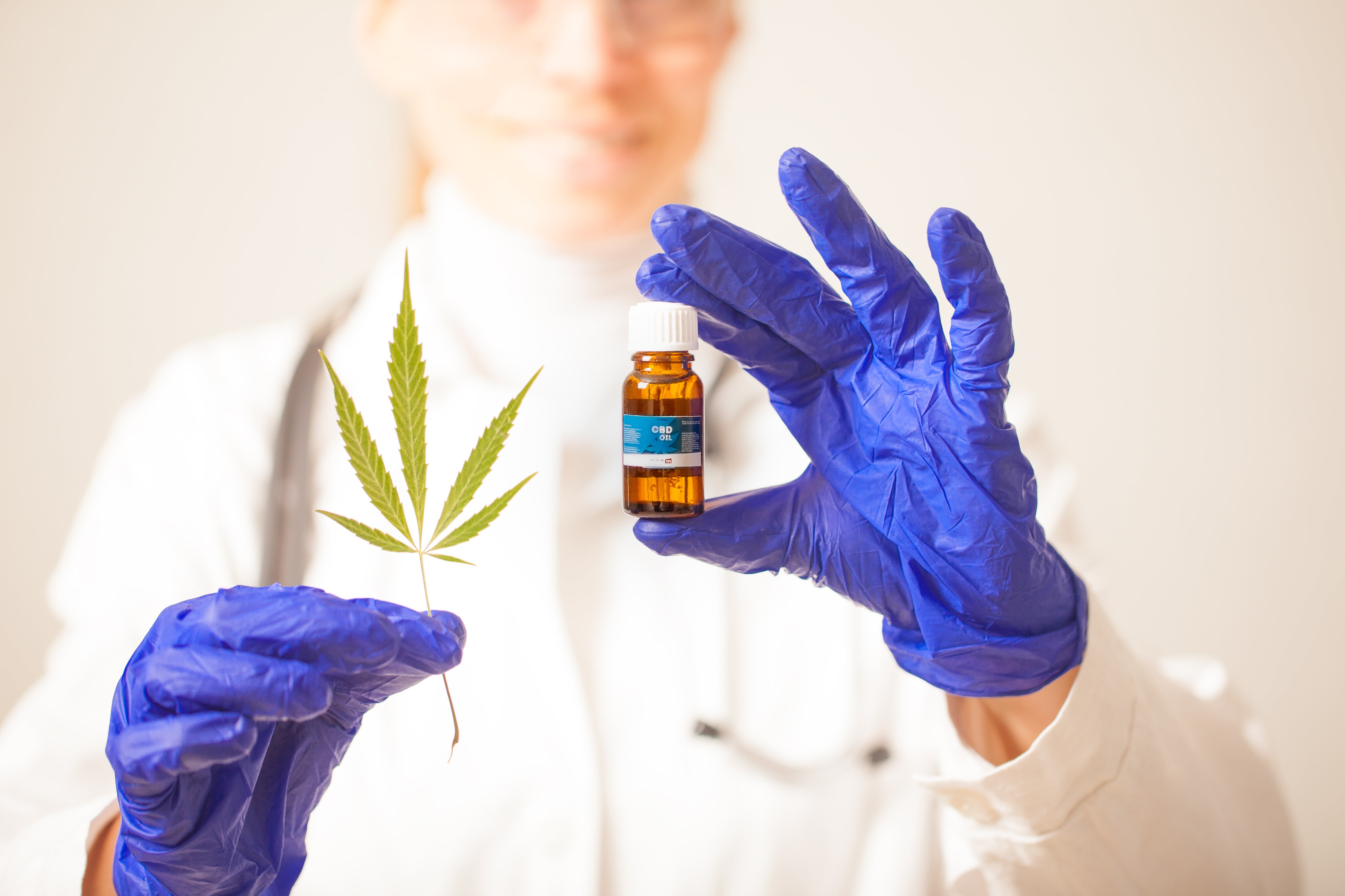 A gloved scientist with a vial of CBD and a hemp leaf. 'Full spectrum' extracts contain more cannabinoids, terpenes, and other beneficial chemicals found in hemp & cannabis.