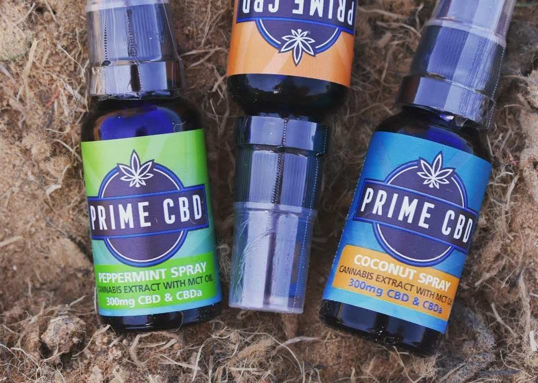 Three bottles of different flavors of Prime CBD oil spray rest against a natural backdrop.