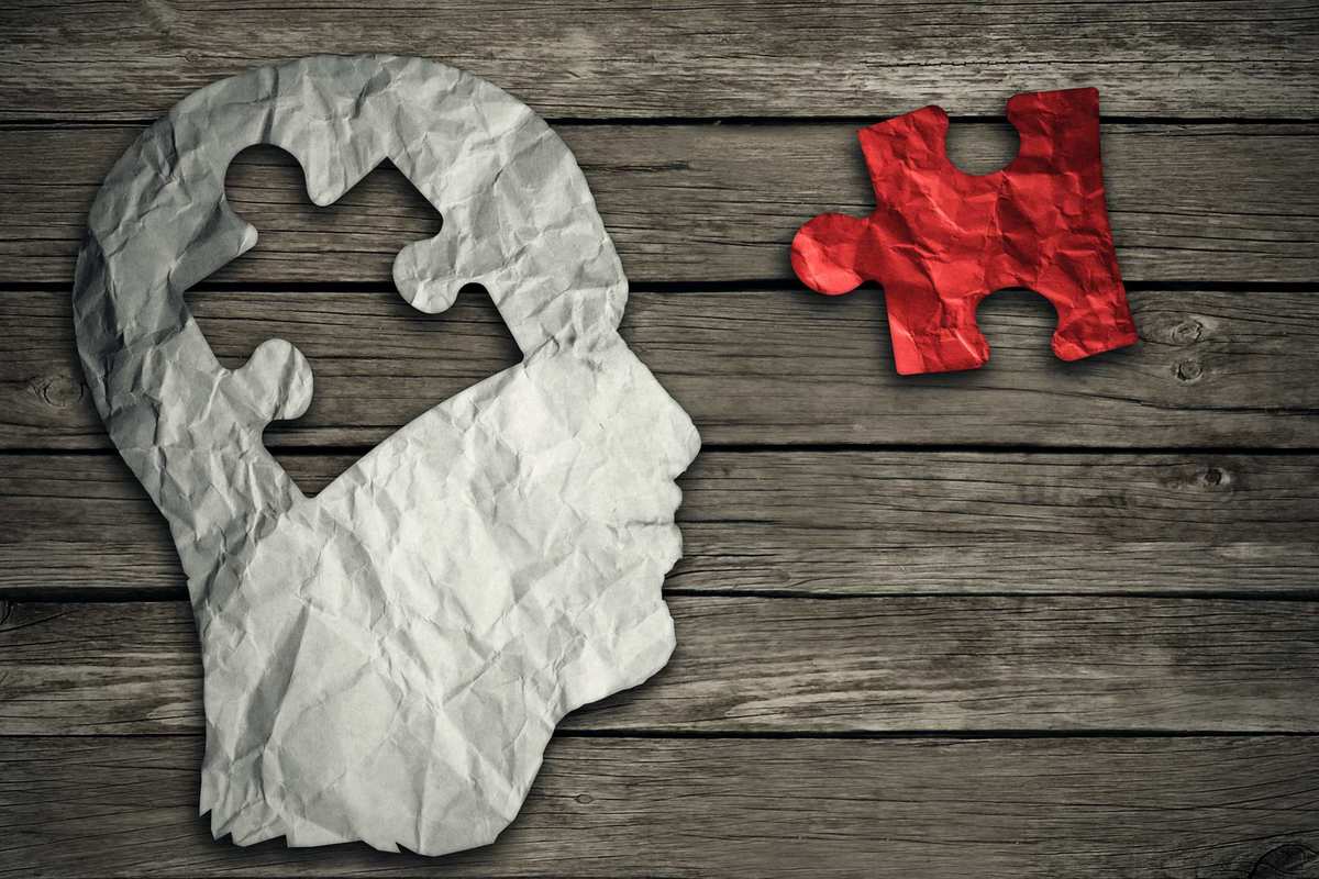 A white paper cutout of a human head, missing a puzzle piece shaped hole, sits on a wooden surface. The puzzle piece, colored red, sits nearby. Though still theoretical, clinical endocannabinoid deficiency could be a common contributor to numerous conditions, from fibromyalgia to migraines.