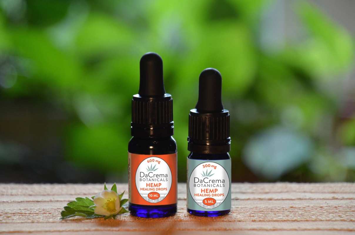 DaCrema Botanicals Hemp Healing Drops sit on a wooden counter, against a green natural background in the distance.