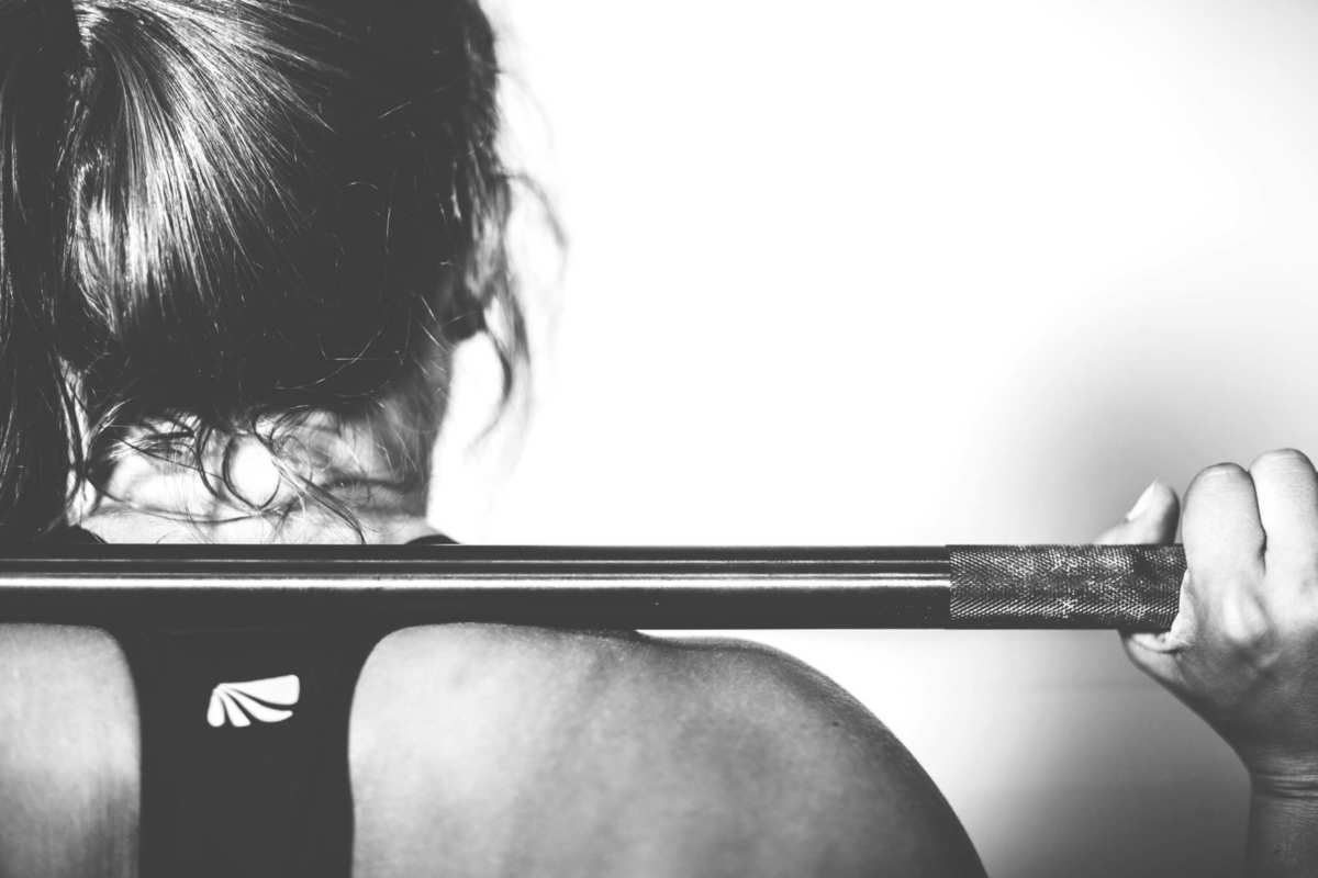 A woman seen from behind holding a weight on her shoulders. Some top athletes are now working out with CBD. CBD oil can reduce the effects of anxiety and promote more restful sleep, all of which promote a better workout. 