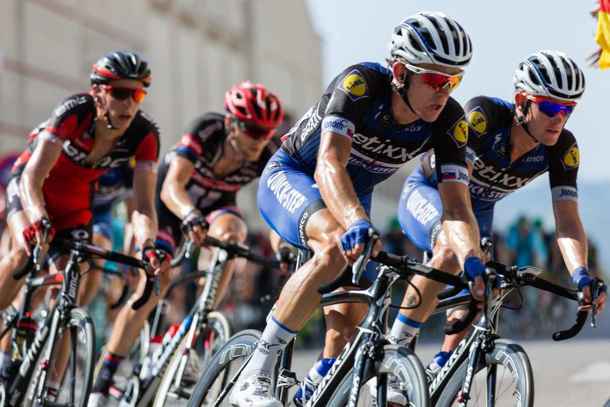 Cyclists race on a roadway in a tight pack, wearing sponsored pro cyclist gear and helmets. Some endurance athletes use CBD to reduce their dependence on pharmaceutical painkillers to relieve the soreness of workouts.