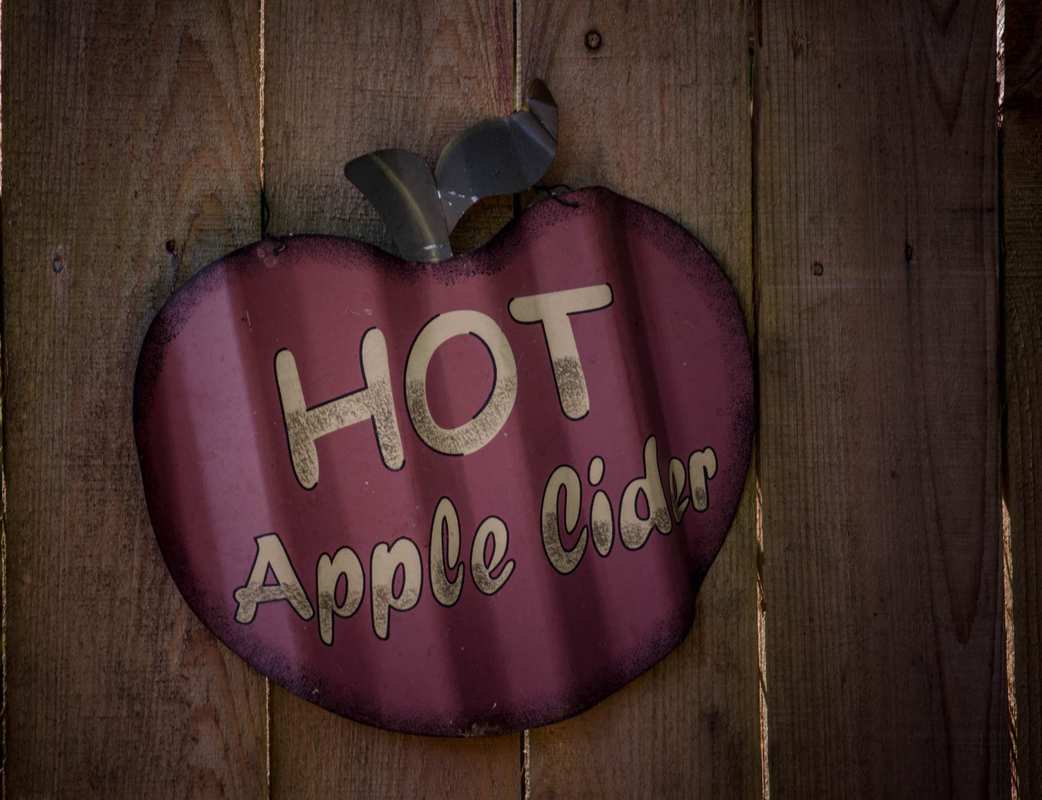 An antique "Hot Apple Cider" sign, shaped like an apple, painted on a wooden fence. Our hot CBD mulled apple cider will enhance those autumn vibes and help you relax during the busy holiday season.