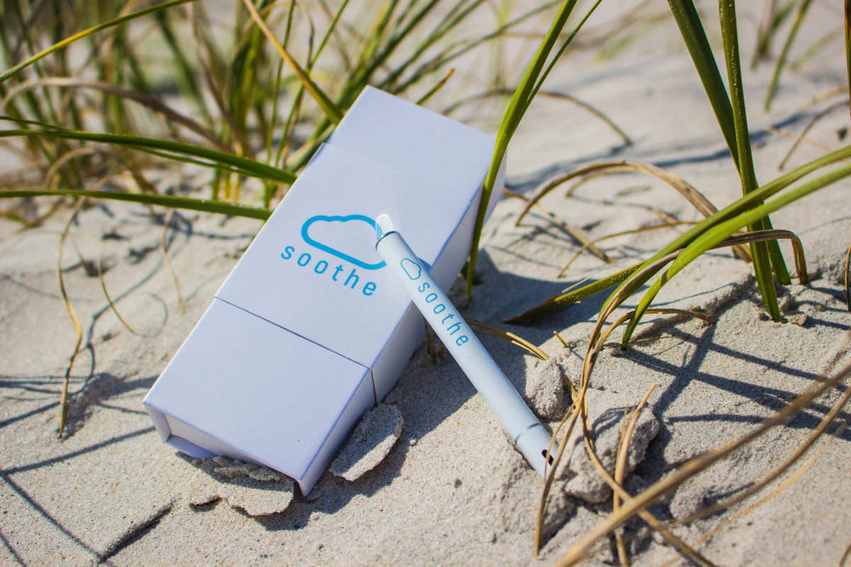 Soothe Puff CBD Vaporizer is a simple, elegant and delicious way to vape CBD on the go. Soothe Puff CBD Vaporizer, a white e-cig style disposable vaporizer, sits on a grassy sand dune next to its elegant white box.