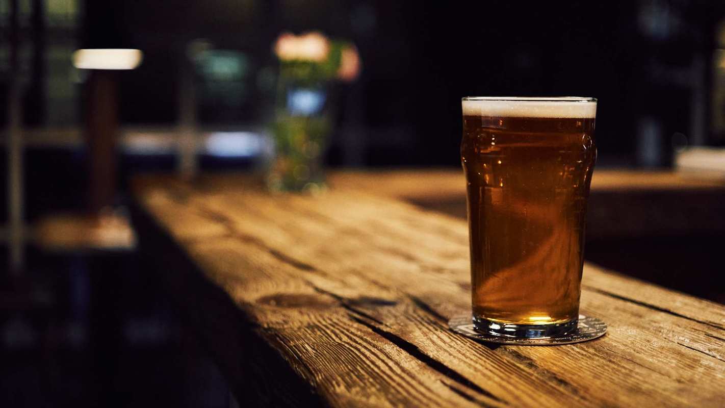 A pint glass of dark beer sits on a rustic bar top in a darkened bar. While hemp makes an enticing beer ingredient, craft hemp beer brewers face legal and regulatory hurdles before they can bring their brews to market.