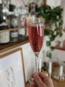 A hand holds a pink cocktail in a champagne glass. Our fizzy CBD drink will help elevate your New Years Eve, or any special occasion!