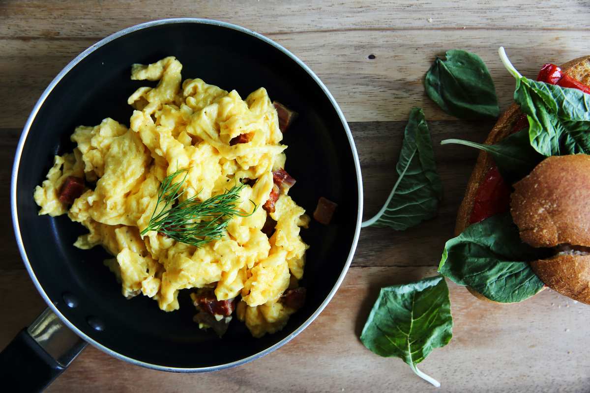 A pan of scrambled eggs with added herbs. Creating a delicious hemp breakfast might be as simple as adding hemp hearts or infusing CBD oil into the butter you use to make eggs.