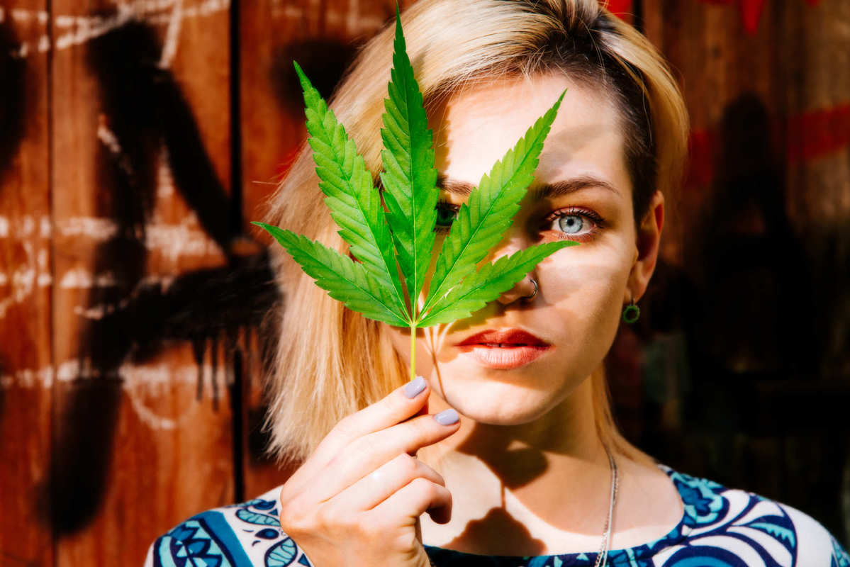 A woman poses with a hemp leaf in hand, partially obscuring the right side of her face. Haddayr Copley-Woods believes everyone has a right to find relief from pain and discomfort. For her, the first step was to research CBD.