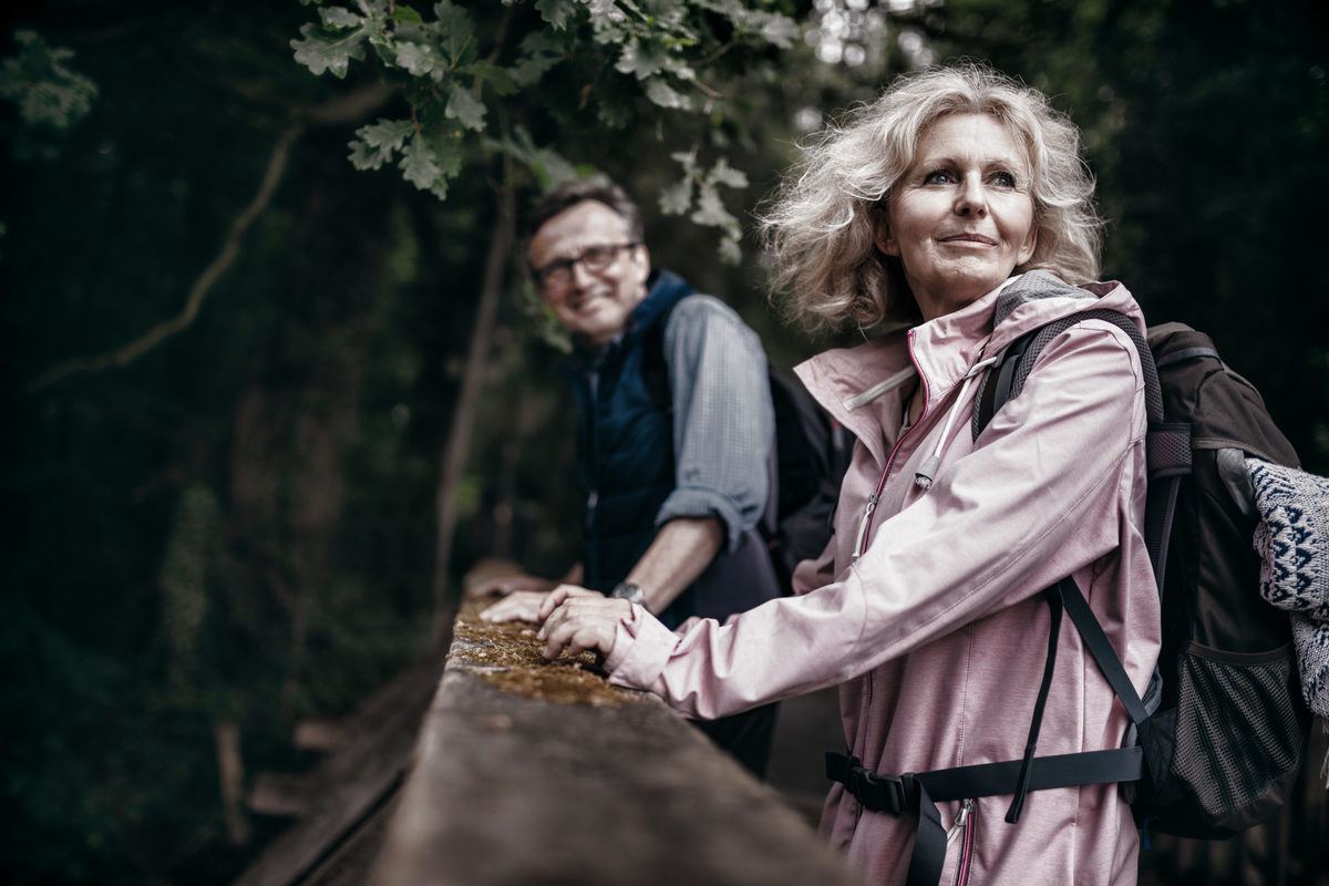 A senior couple pause by a rock wall as they enjoy a hike in the woods. Life Patent CBD-A Oil offers unique benefits that could help people of all ages maintain an active lifestyle.