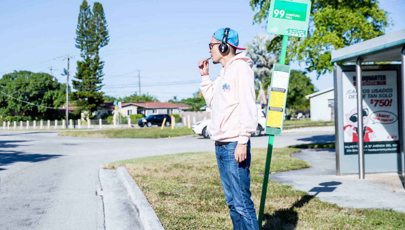 A person vapes CBD while waiting at a suburban bus stop, wearing headphones, jeans and a hoodie. Due to it's absorption rate, CBD vape oil is a fast, easy way to get relief from numerous troubling symptoms. (Photo: Medix CBD)