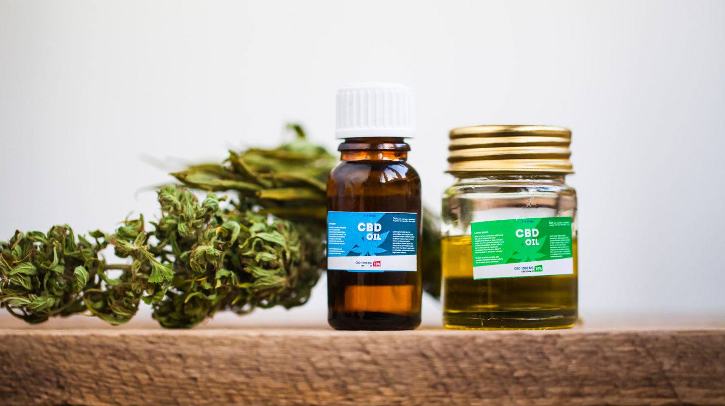 A hemp bud, and two bottles of CBD oil sit on a wooden tabletop. Unfortunately, CBD and hemp brands will continue to face problems online until the stigma around the plant disappears.
