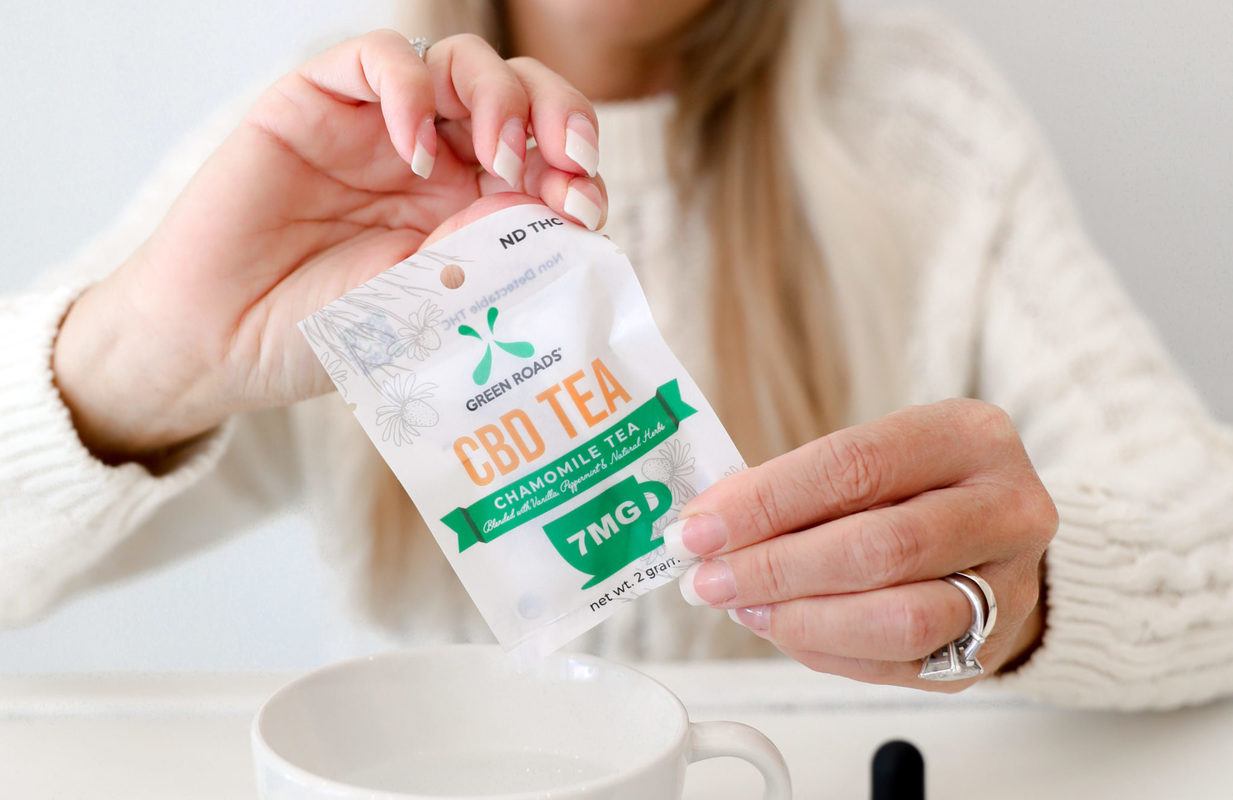 A woman opens a packet of CBD tea to pour it into a tea cup. Some benefits of CBD for the elderly include reducing pain and symptoms of stress.