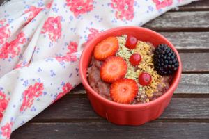 A bowl of oatmeal with fruit, hemp seeds and chia seeds added sits on a wooden picnic table near a folded flower print tablecloth. Hemp oatmeal can supercharge your mornings and help you eat healthier in 2019.