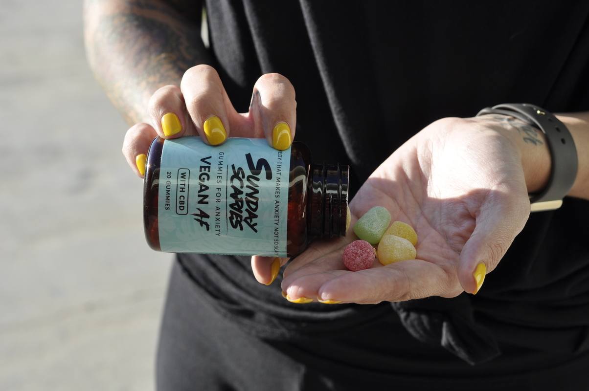 A person in dark clothes with bright yellow nail polish pours Sunday Scaries Vegan AF CBD Gummies into the palm of their hand.
