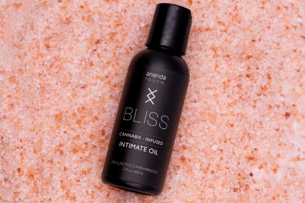 Ananda Touch Bliss Oil from Ananda Hemp, seen against a background of rosy pink bath salts. Ananda Touch Bliss Oil is designed to enhance bloodflow and reduce pain. Used as a lube, Bliss Oil makes erotic encounters slippery and more fulfilling.