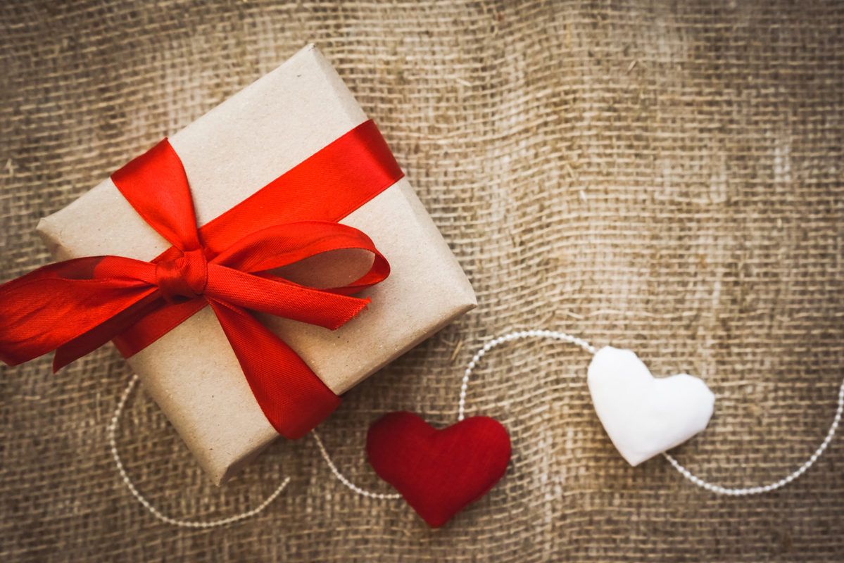 Ministry of Hemp Official Valentine's Day CBD Gift Guide. A gift wrapped with a red ribbon and decorated with hearts on a string, sitting on a fabric background.