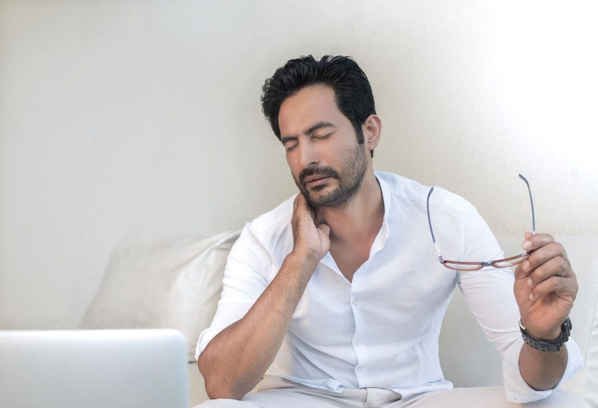 A seated man holds his glasses in one hand while wincing and holding his neck, as if in pain, with the other. Both CBD and THC can relieve symptoms of chronic pain and inflammation in unique ways, both alone and working in concert with other cannabinoids.