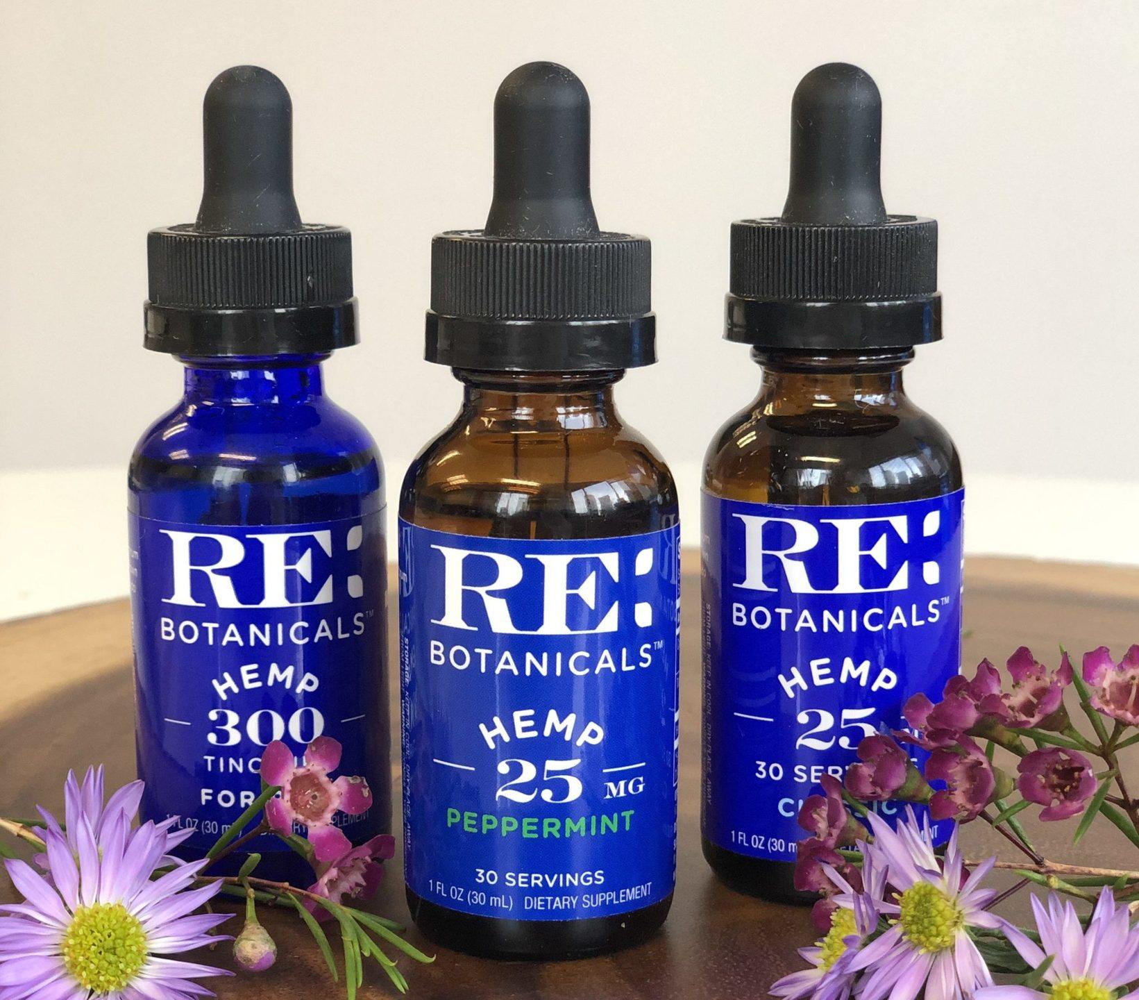 RE Botanicals Hemp Tincture tastes great, and left our reviewers feeling relaxed. Photo: RE Botanicals Hemp Tincture bottles on top of a wooden surface decorated with flowers.