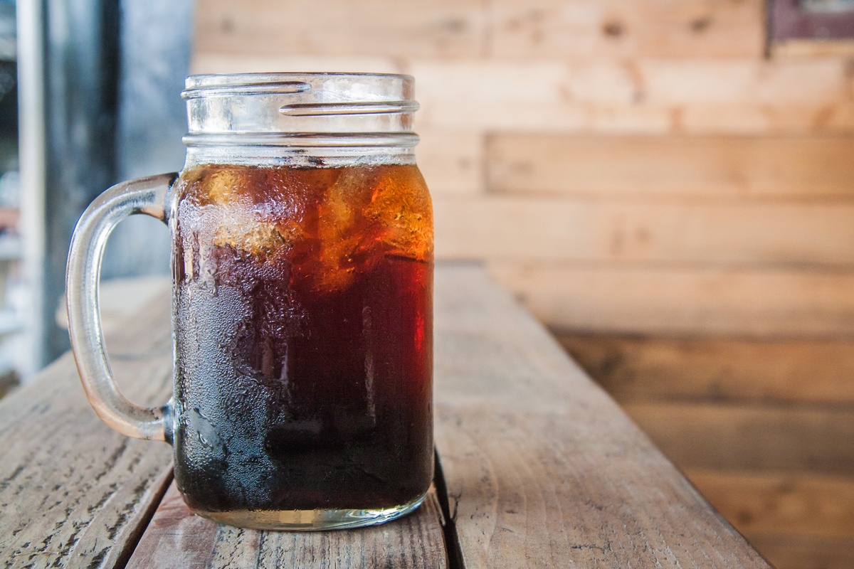 Our hemp oil cold brew recipe is easy, delicious, energizing, and even good for you. Photo: A mason jar-style mug of cold brew coffee with ice cubes rests on a rustic wooden counter.
