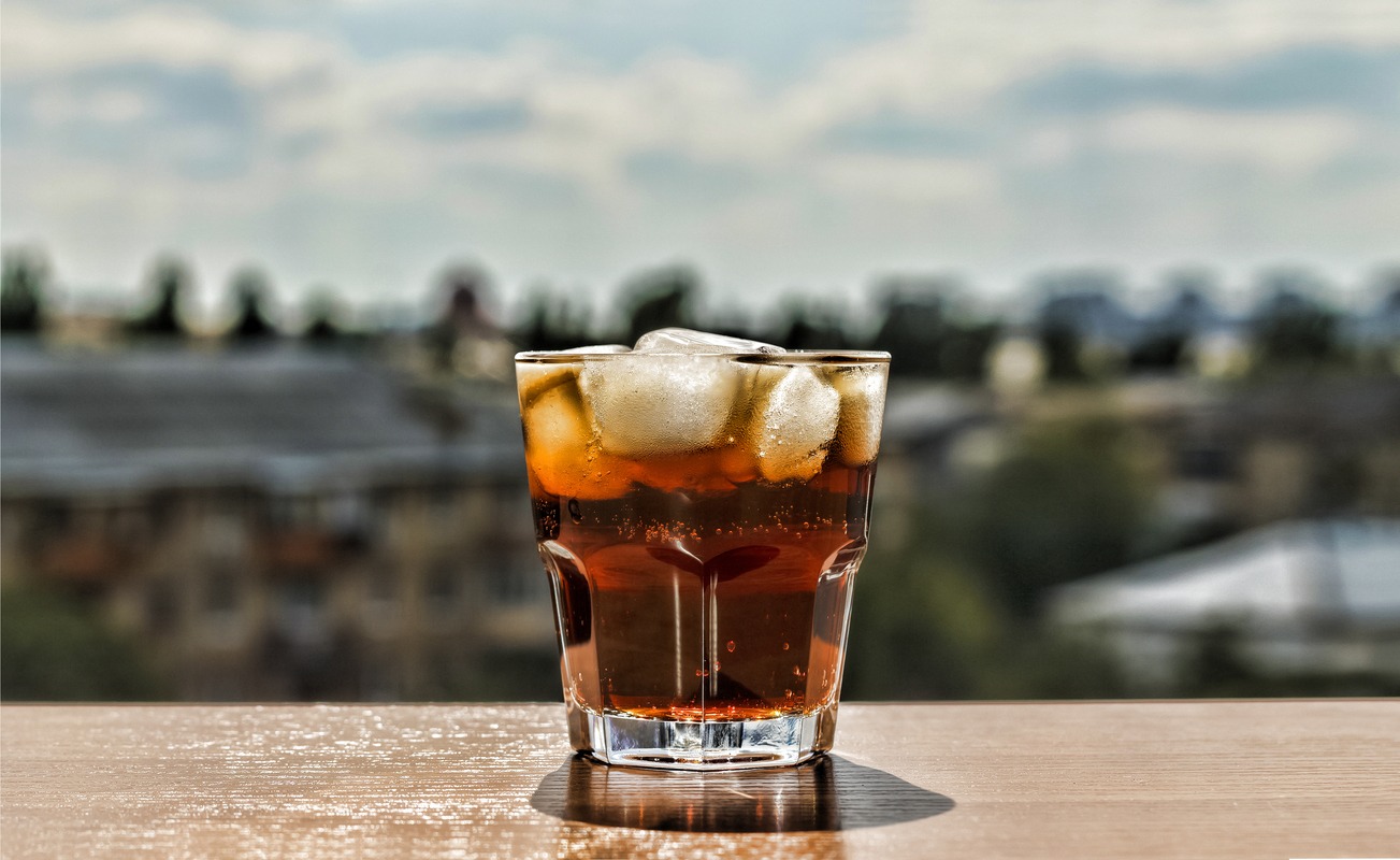 Even the water used by Wee Hemp Spirits is carefully selected to enhance the flavor and effectiveness of their CBD liquor. Photo: A rum and coke with ice in a lowball glass, sitting on a table at the edge of a blurry nature scene.