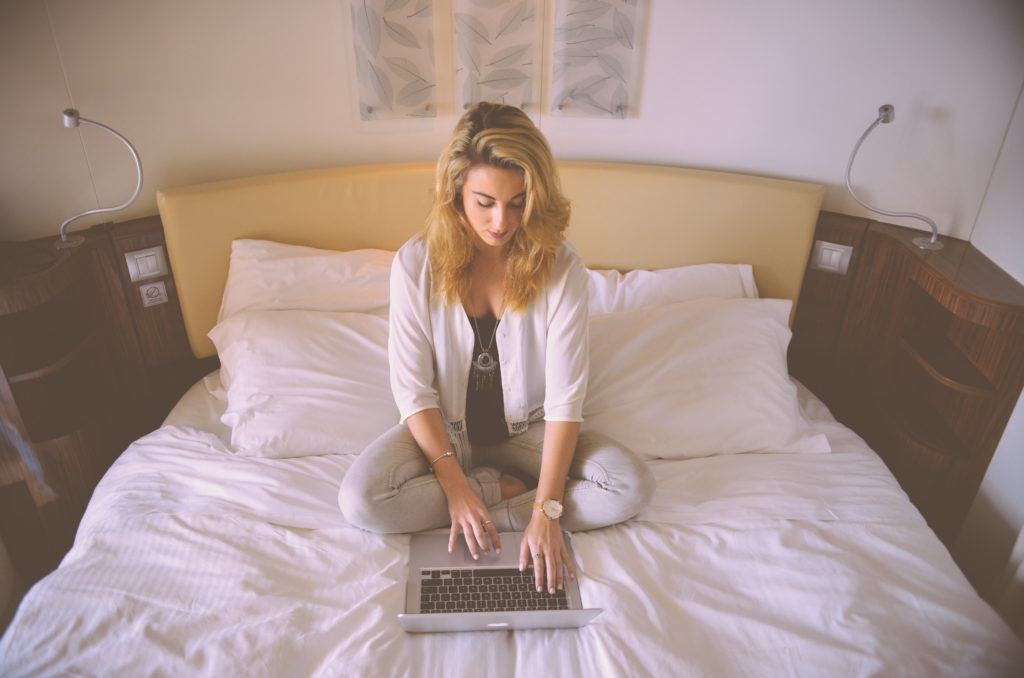 A woman sits cross legged in bed working on a laptop. CBD seems to be very safe in adults, and may show promise for CBD treatment.