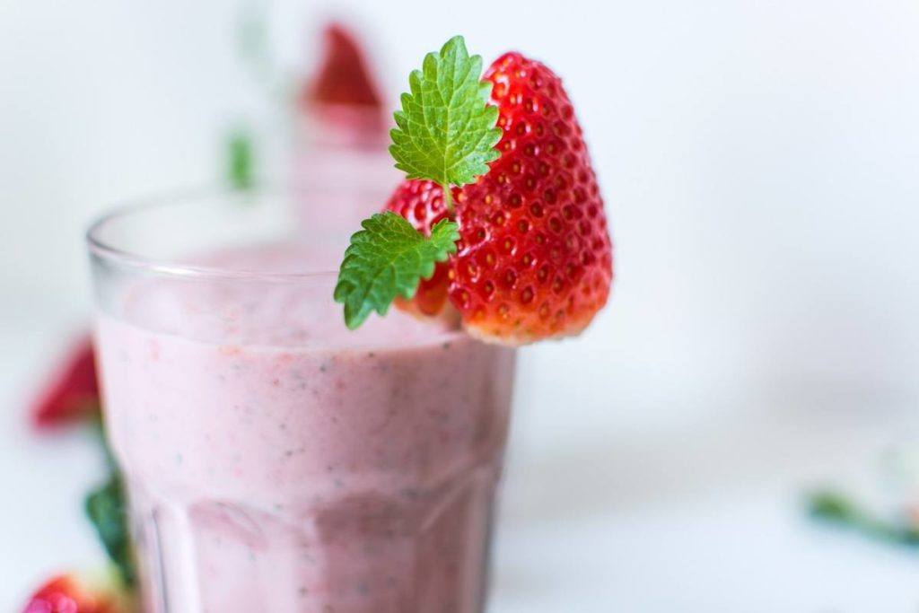 A berry hemp protein smoothie in a drinking glass, garnished with a strawberry.