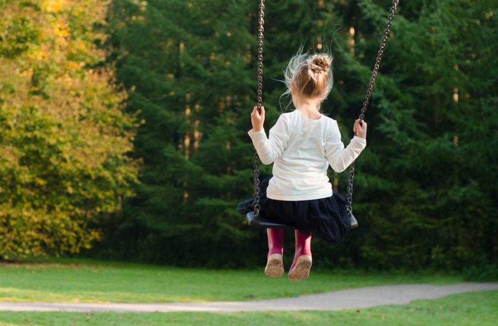 Seen from behind, a girl swings on a swingset alone outdoors. Numerous factors contribute to ADHD, including both environmental and genetic contributors.