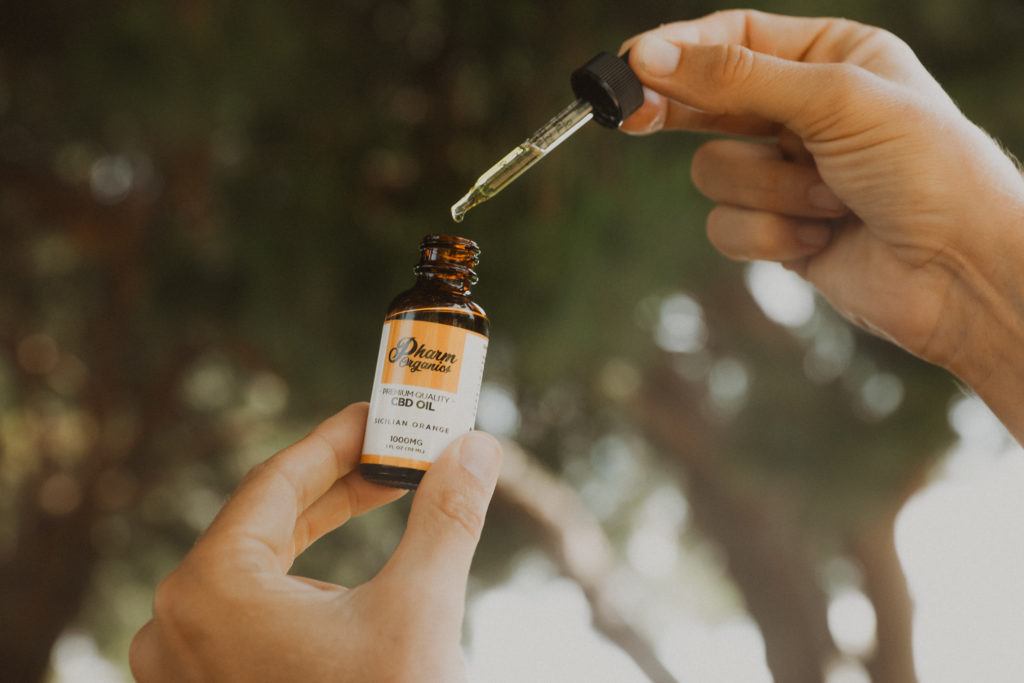 Photo: A person's hand holds Pharm Organics CBD Oil Sicilian Orange flavor, in 1000mg strength, with the bottle in one hand and the dropper in the other.