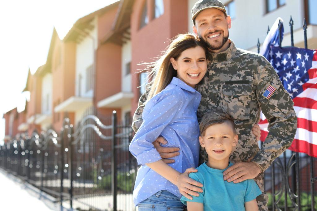 CBD assistance programs offer discounted rates on CBD oil products to veterans, the disabled, low income households, seniors, and other groups. Photo: A soldier with his family, including a wife and son, posing outside a row of apartments with an American flag.