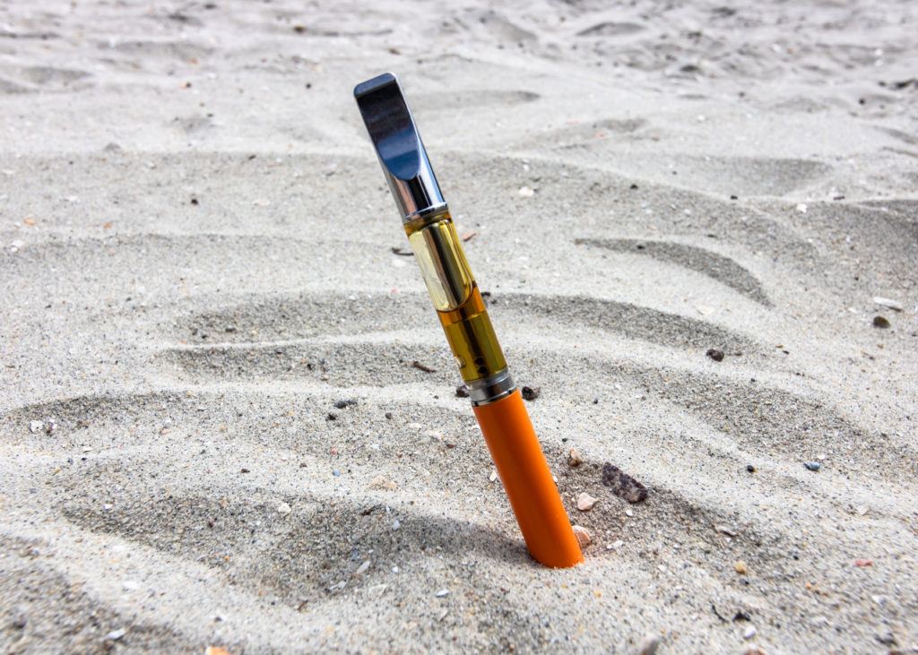 We talked with an expert on hemp quality about CBD vaping safety and hemp certification. Photo: A vaping device, including battery and cartridge of cannabis oil, in the sand at the beach.