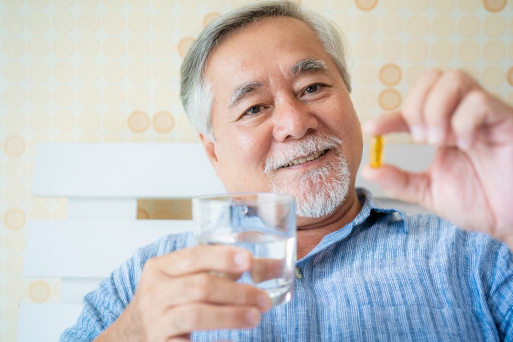 From reducing inflammation to helping balance the endocannabinoid system, we took a closer look at the anti-aging properties of CBD. Photo: A mature man holds up a supplement capsule, smiling, with a glass of water in the other hand.