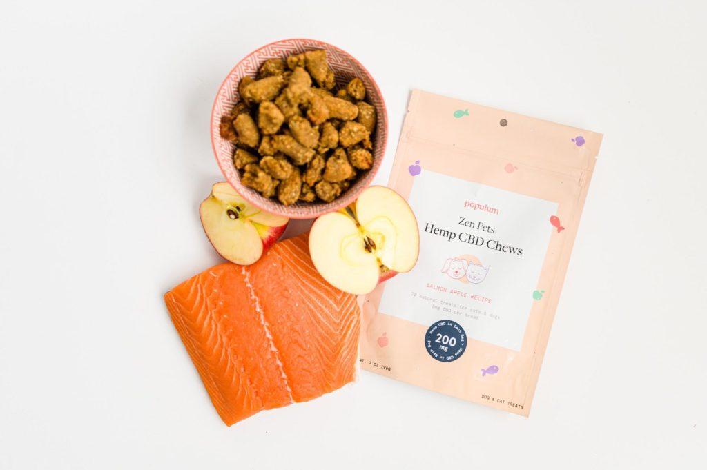 We were impressed by the quality ingredients in Populum Zen Pet Hemp CBD Chews. Photo: Populum Zen Pets Hemp CBD Chews in a bowl, and pouch, posed with key ingredients from the treats: salmon and apple halves.