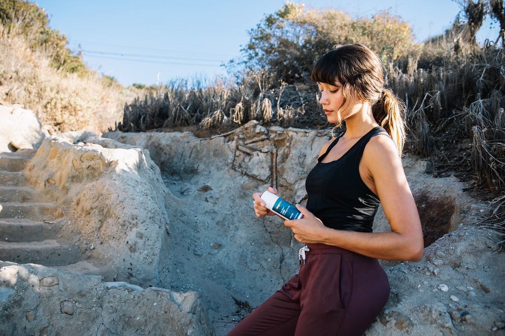 Photo: A jogger leans against a natural stone wall while holding Vitagenne CBD Cooling Cream.