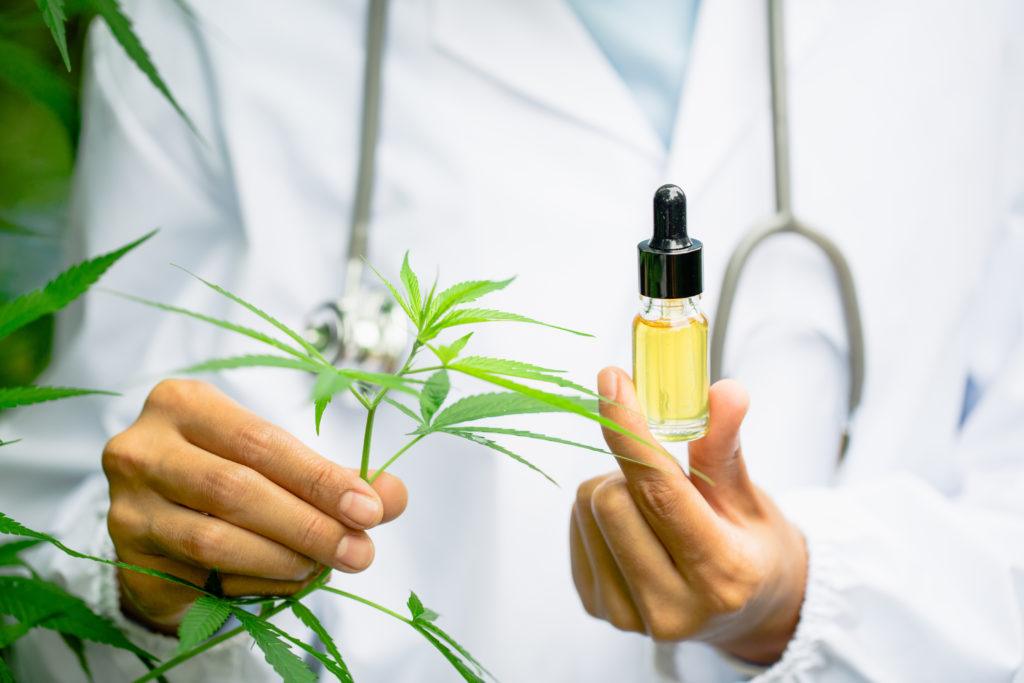 Epidiolex, a prescription epilepsy drug based on CBD, complicates the FDA's treatment of over-the-counter CBD supplements. Photo: A researcher in a lab coat and stethoscope holds a hemp leaf in one hand and a bottle of hemp extract in the other.