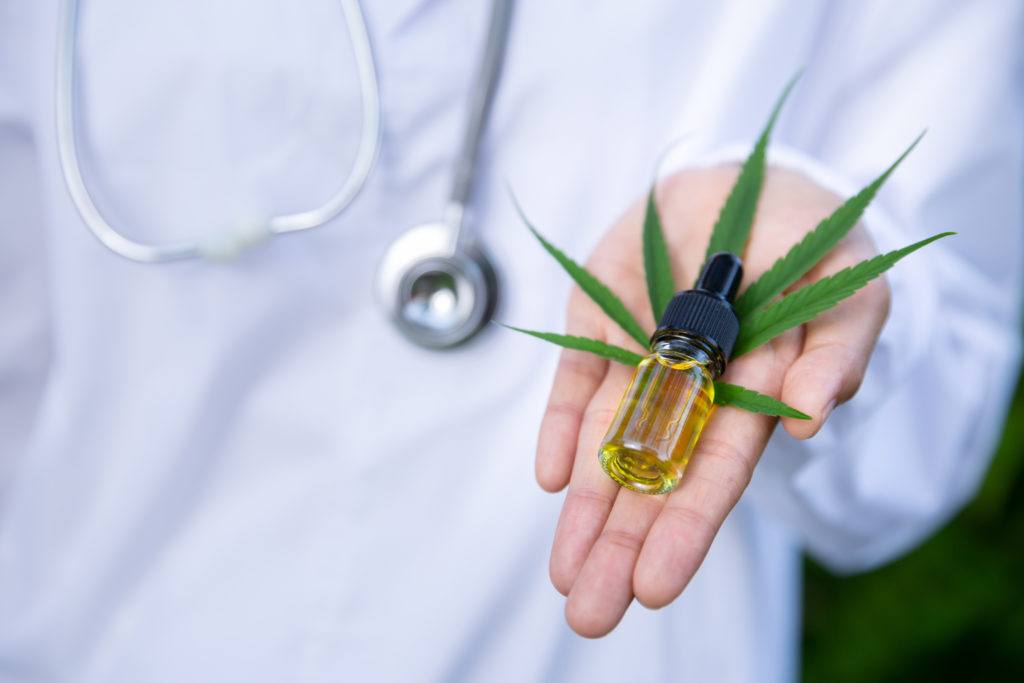The FDA doesn't currently regulate CBD, but they do act against brands that make unrealistic health claims. Photo: A researcher in a lab coat and stethoscope holds a hemp leaf and a vial of CBD extract.