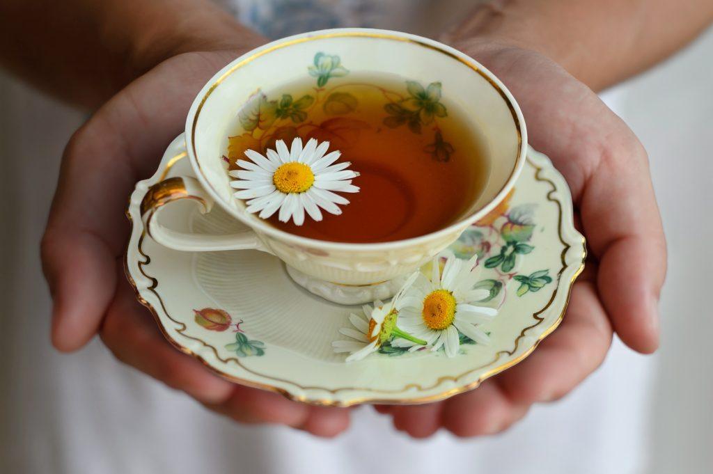 Chamomile could be one of the best known natural sleep aids. Photo: A person holds a teacup and saucer in cupped hands. In the cup is chamomile tea, garnished with fresh chamomile flowers.