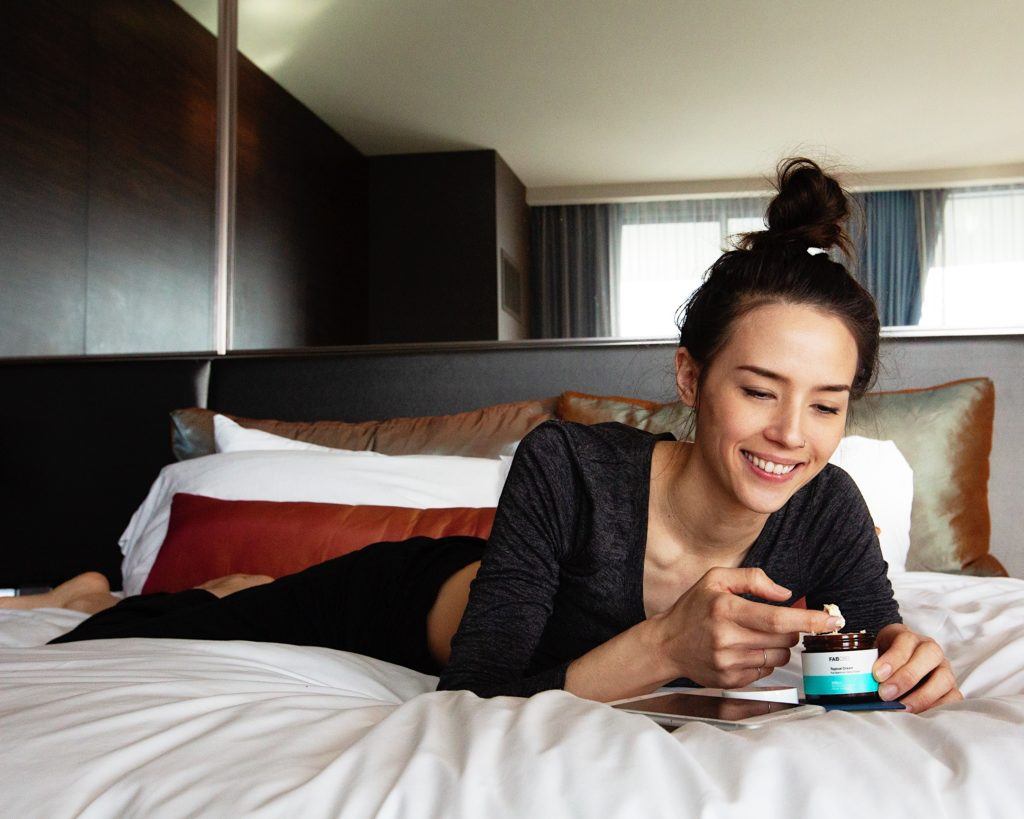 For some beginners, other forms of CBD such as topicals, edibles like gummies, or CBD capsules might seem more accessible than oil. Photo: A woman reclines in bed as she begins to apply a CBD topical onto her fingertip.