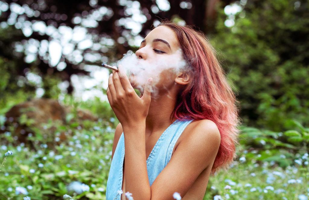 Photo: A woman exhales as she smokes a hemp flower joint in a field of wildflowers.