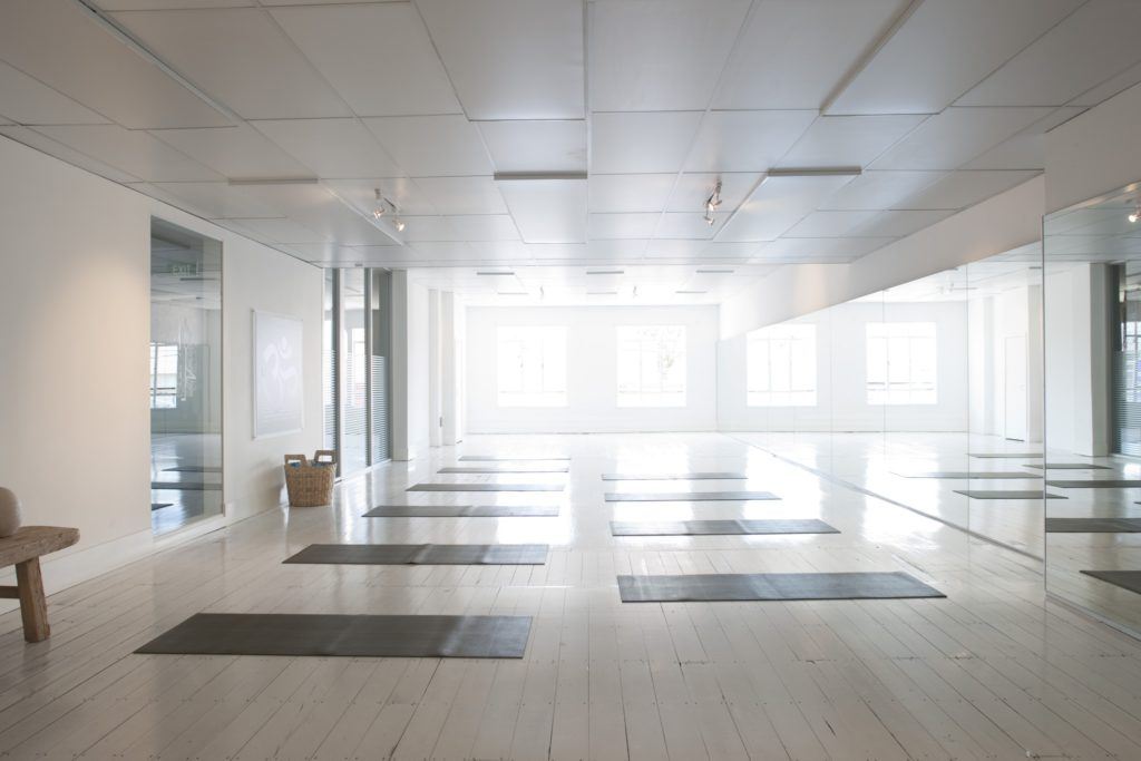 Photo: An empty, sunlit yoga studio, with yoga mats ready for students. 