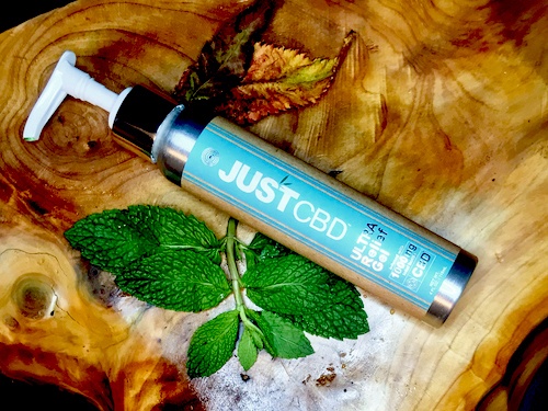 A bottle of JustCBD topical cream arranged on a wooden surface with mint leaves.