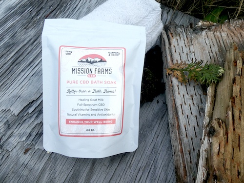 Mission Farms Bath Soak arranged outdoors on a log, with a white rolled up towel.
