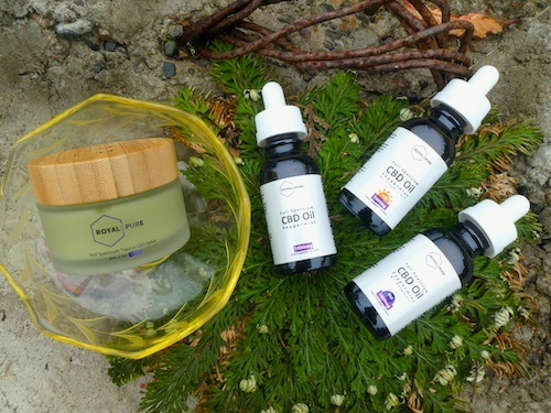 Royal & Pure products arranged outdoors on a green organic background, including a topical CBD balm and CBD tinctures.