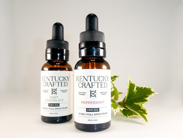 Two Kentucky Crafted CBD oil tinctures with a decorative sprig of ivy.