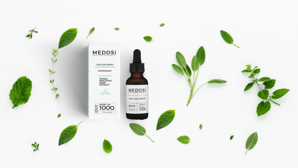 Medosi Tincture Drops bottle and box surrounded by decoratively scattered peppermint leaves.