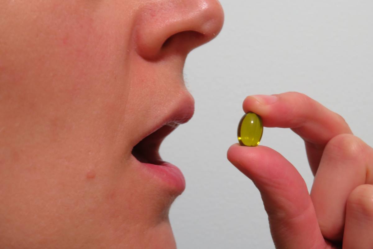 The quality of CBD oil makes a difference when it comes to side effects. Photo: A closeup of a person's mouth as their take a CBD capsule held in their fingers.