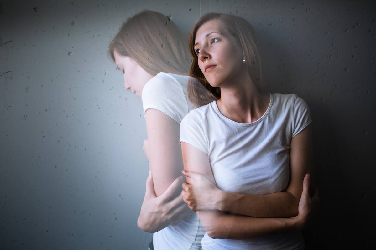 CBD isn't a cure for anxiety, but many consumers report major relief from some of its most troubling symptoms. Science is beginning to support this use. Photo: A double exposure-style photo showing two images of a white woman in a white t-shirt, hugging herself with anxiety, shoulders hunched.
