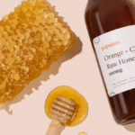 Populum Orange + CBD Honey posed with a honeycomb and a wooden honey dipper that's dripping with honey.