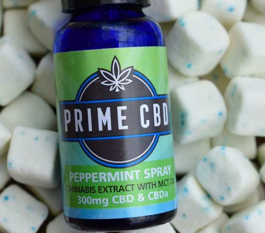 A bottle of Prime CBD oil spray rests on a bed of peppermint breath mints.