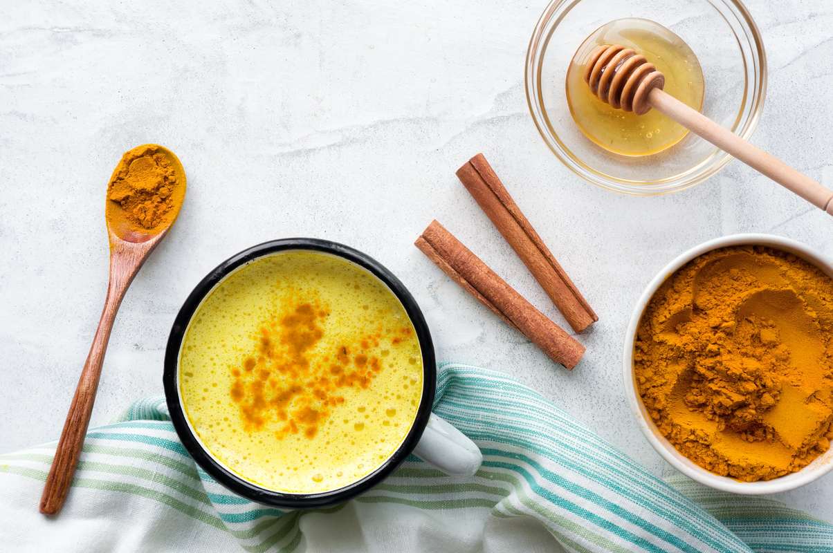CBD golden milk is the perfect way to make this popular drink even better. Photo shows golden milk in a mug along with ingredients including turmeric, cinnamon and honey.