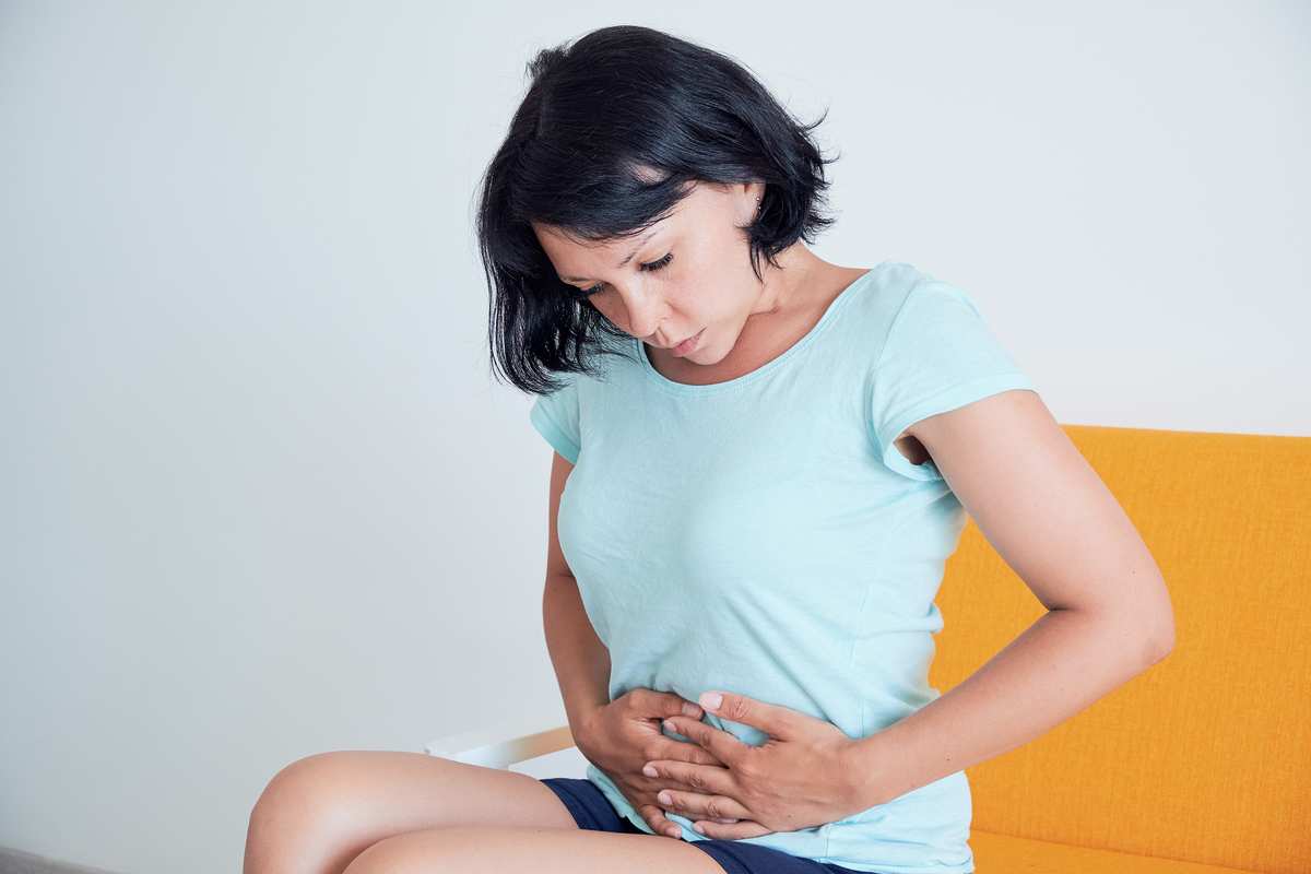 A woman clutches her stomach in pain or discomfort. While research is just beginning, science supports the potential of using CBD oil for Crohn's disease.